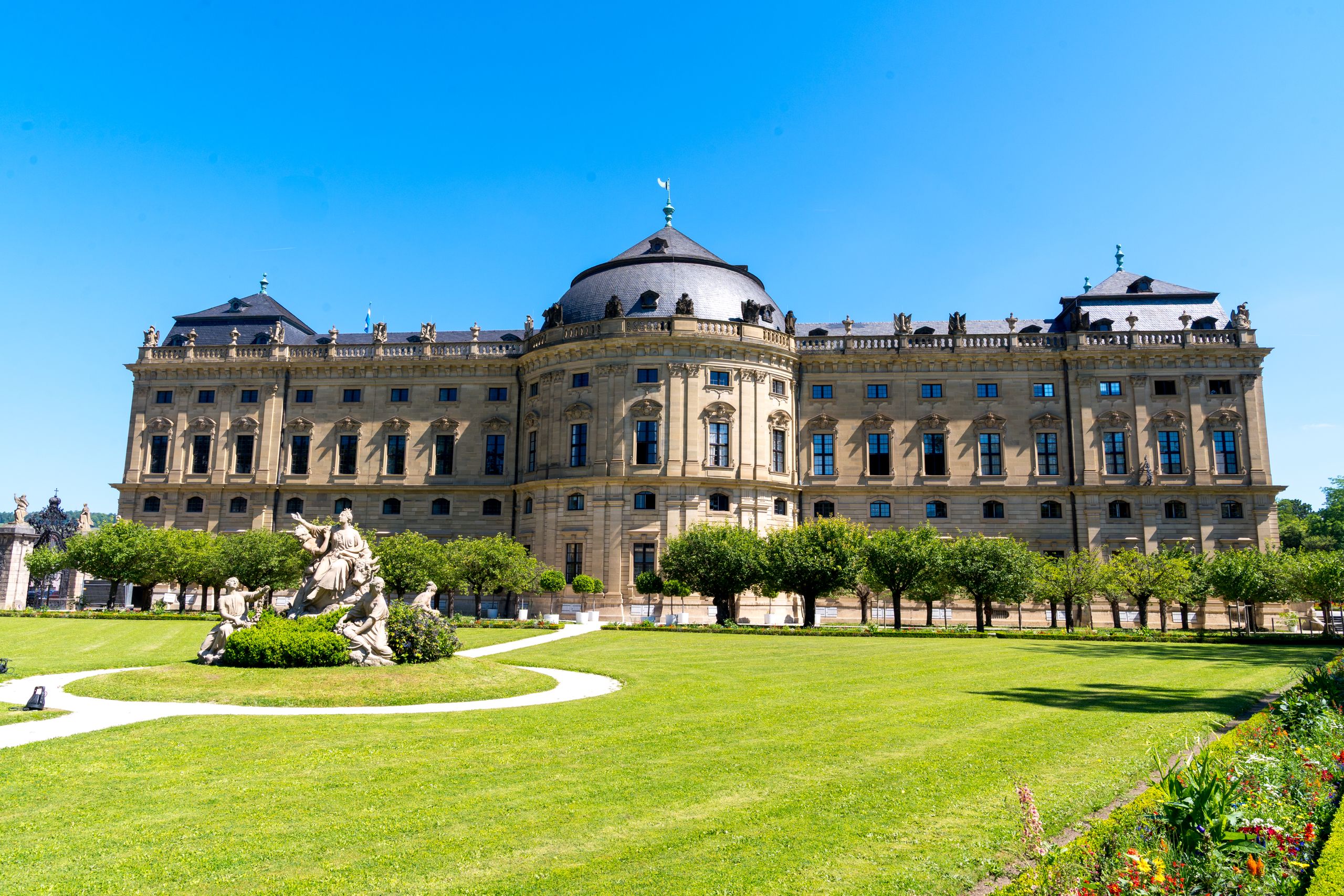 The grand Würzburg Residence showcases Baroque architecture amid well-manicured gardens on a sunny day.